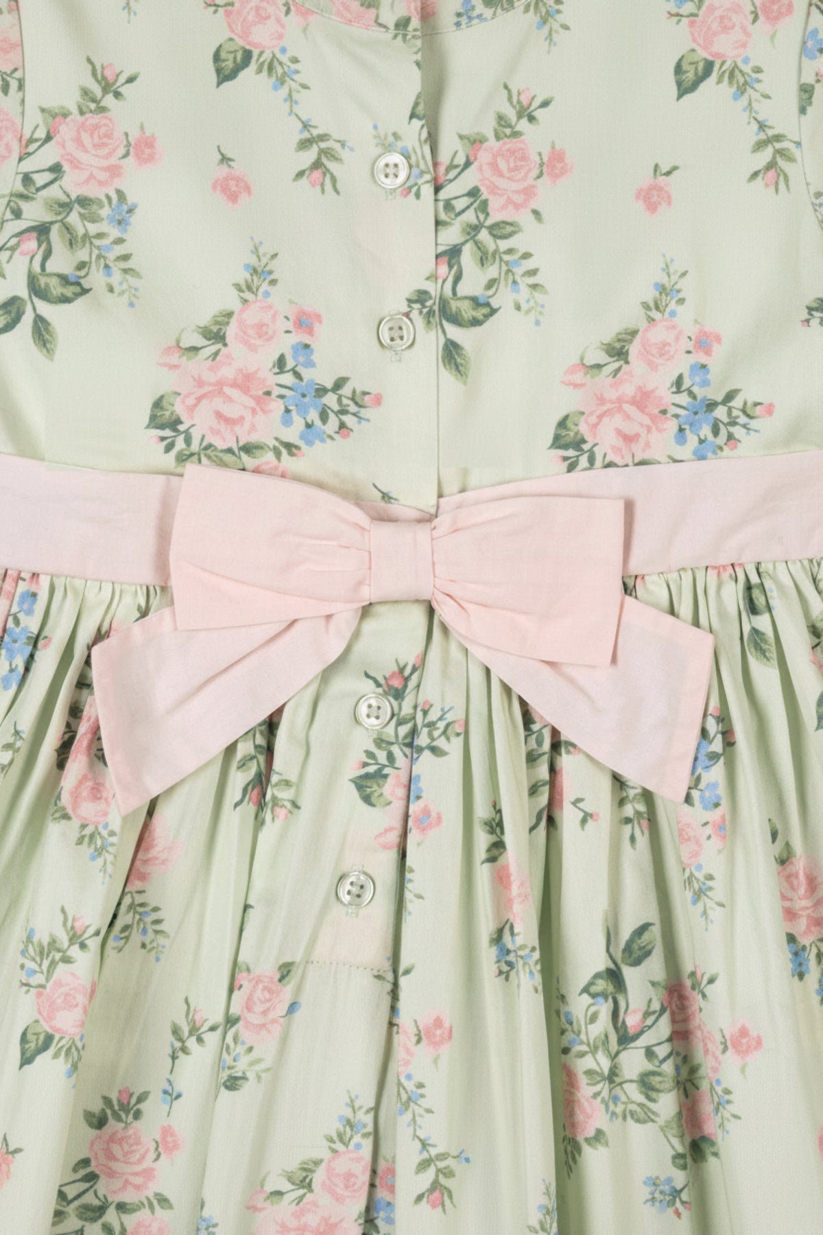A close-up of a floral dress featuring a mint green fabric with pink and blue flowers, a bow detail, and.