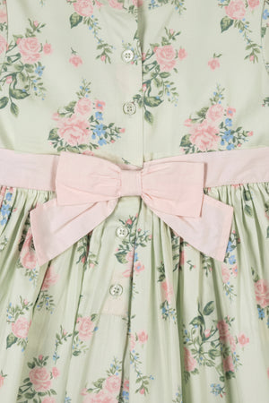 A close-up of a floral dress featuring a mint green fabric with pink and blue flowers, a bow detail, and.
