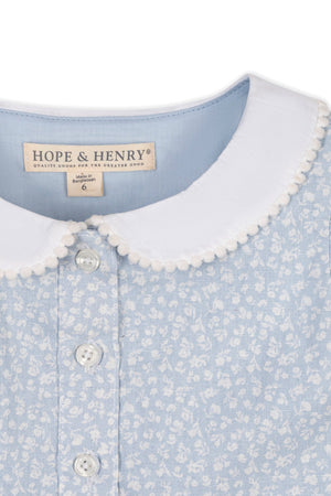 Close-up of a light blue dress featuring a Peter Pan collar with pom-pom trim, delicate floral patterns, and button details, designed by Hope & Henry for toddlers and kids.