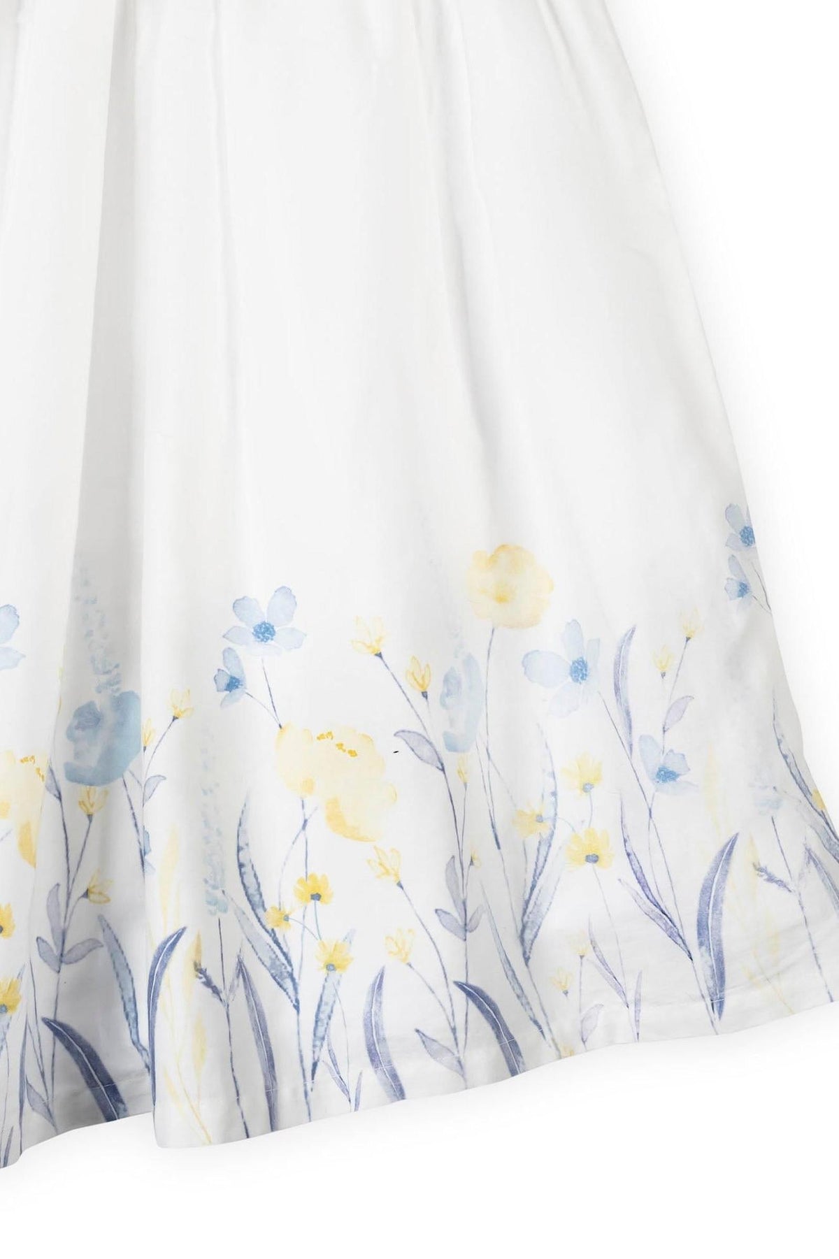 Close-up of a soft white dress featuring a watercolor floral print in light blue and yellow at the hem.