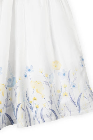 Close-up of a soft white dress featuring a watercolor floral print in light blue and yellow at the hem.