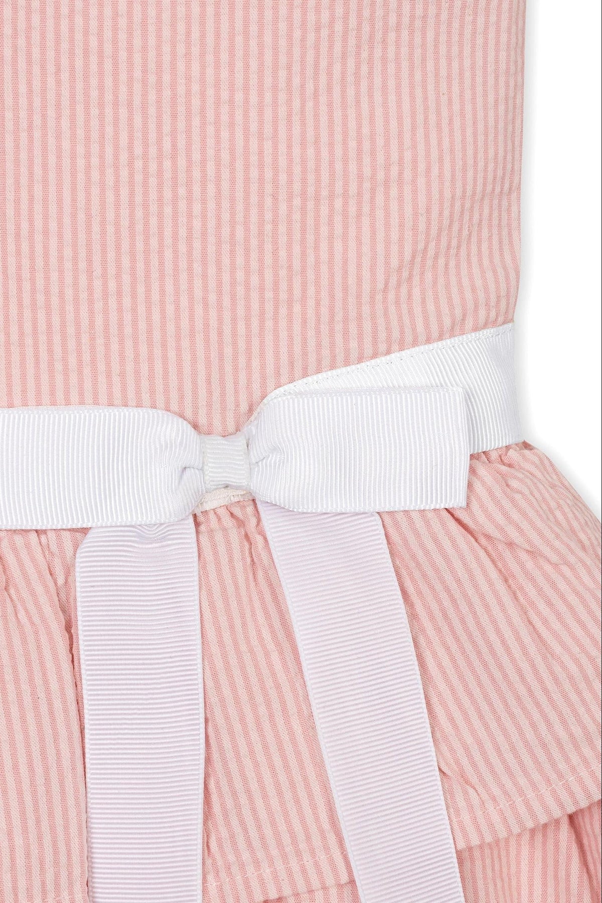 Close-up of a pink and white striped organic cotton dress featuring a ruffled peplum waist and a white bow belt.