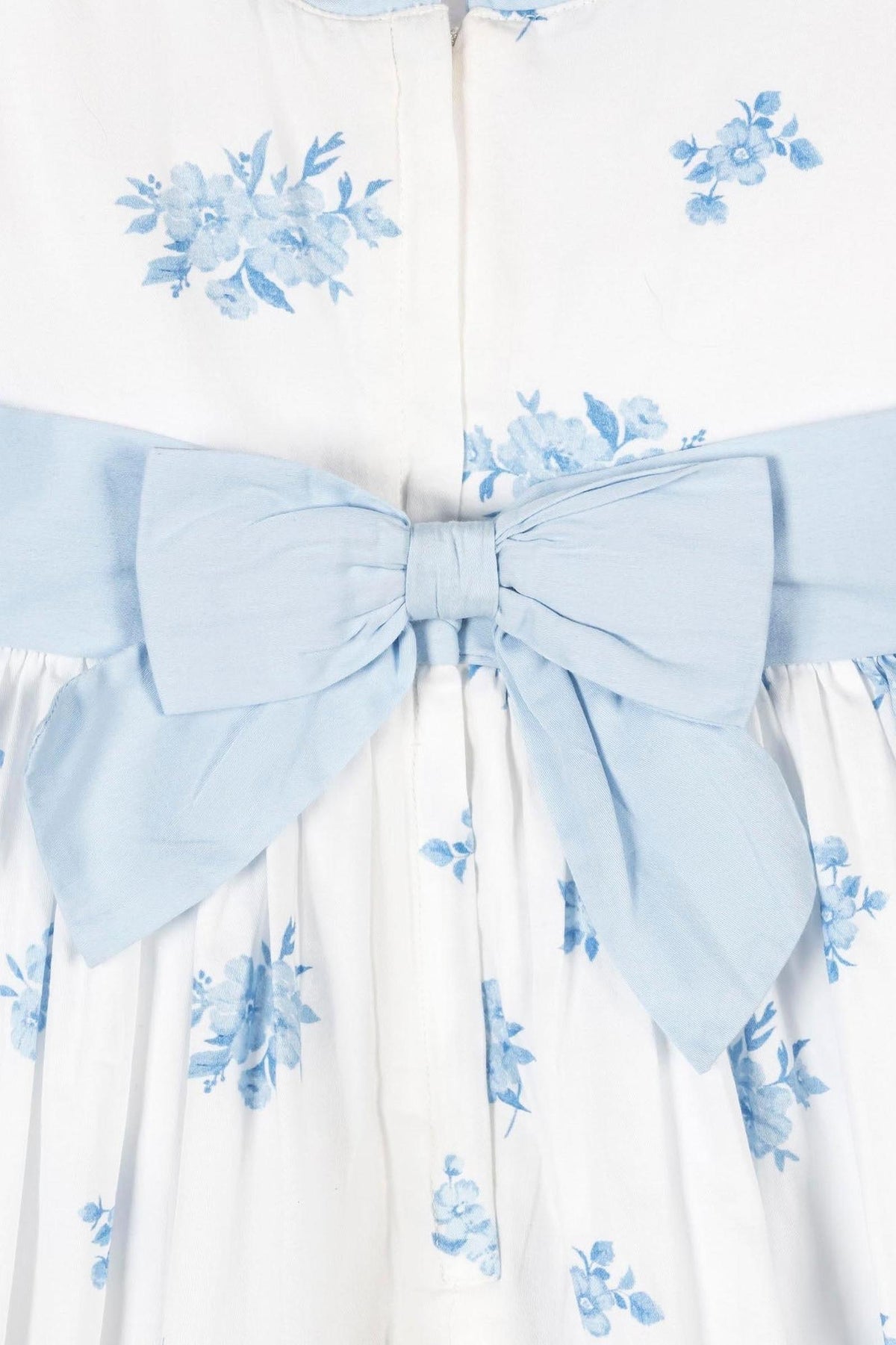 Close-up of a white dress with blue floral patterns and a light blue bow at the waist, showcasing organic cotton.