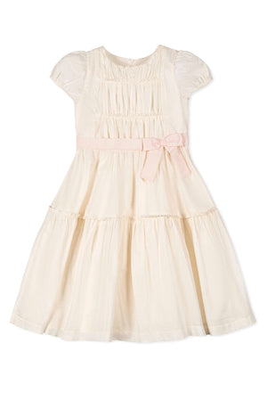 Natural-colored girls dress with puff sleeves, pink waist sash, and tiered skirt made from organic cotton.
