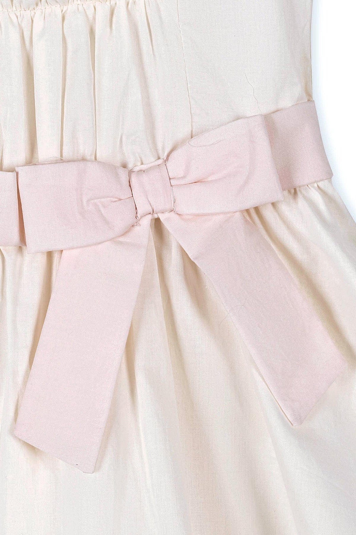 Close-up of a natural-colored dress with a light pink bow at the waist, made of organic cotton fabric.