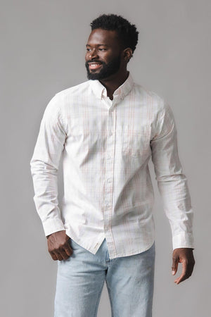 A man smiles while wearing a long-sleeve, button-down shirt in a soft, light-colored Chateau plaid pattern. The shirt features a functional chest pocket and is made from organic cotton.