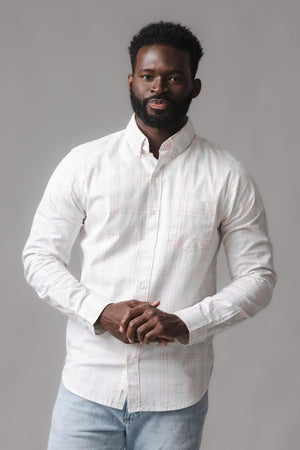 A man is wearing a long sleeve, button-down shirt in a light chateau plaid pattern, made from soft organic cotton. The shirt features a chest pocket and a classic collar.