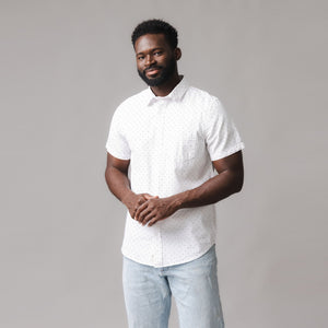 A man stands in a white short sleeve seersucker shirt with a subtle polka dot pattern, paired with light blue jeans.