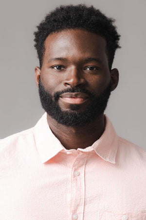 A man with a well-groomed beard is wearing a light pink short-sleeve shirt. The shirt features a subtle seersucker texture, perfect for warm weather and casual occasions.