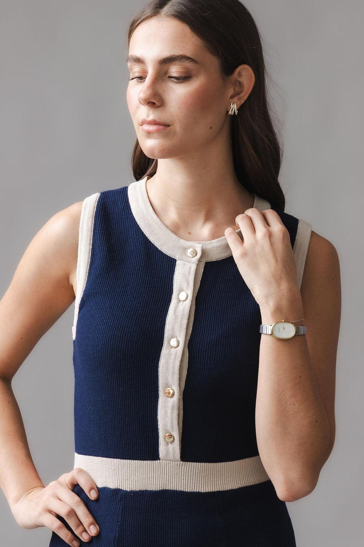 A young woman models a navy organic cotton sweater dress featuring a button front and contrast rib trim. She wears minimal accessories, highlighting the dresss sophisticated and sustainable design.