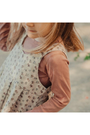 A young girl is wearing a floral corduroy dress over a long-sleeve top, showcasing a soft color palette.