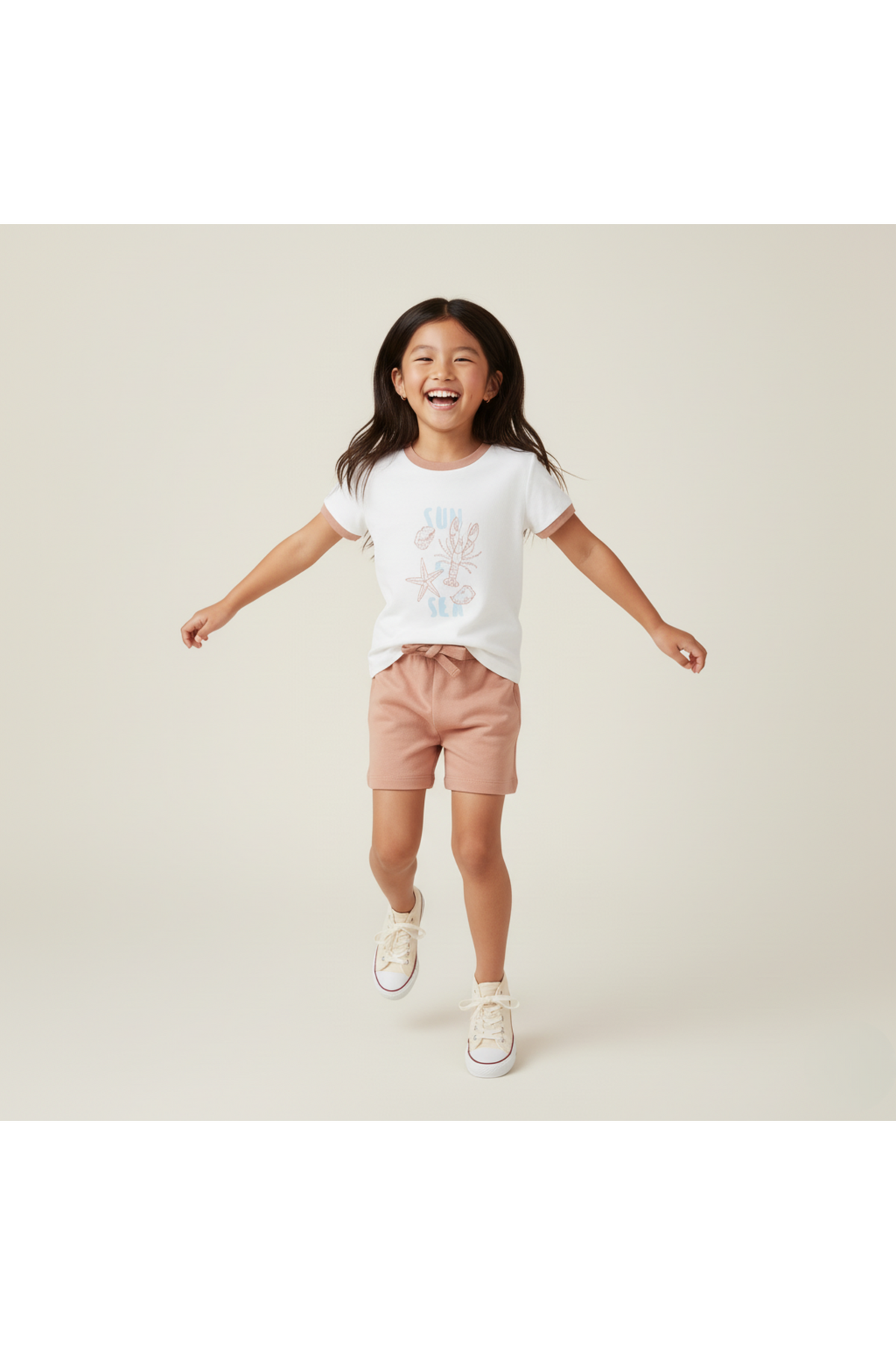 A joyful child wears a white graphic tee featuring a colorful beach design paired with light pink shorts.