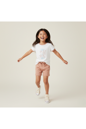 A joyful child wears a white graphic tee featuring a colorful beach design paired with light pink shorts.