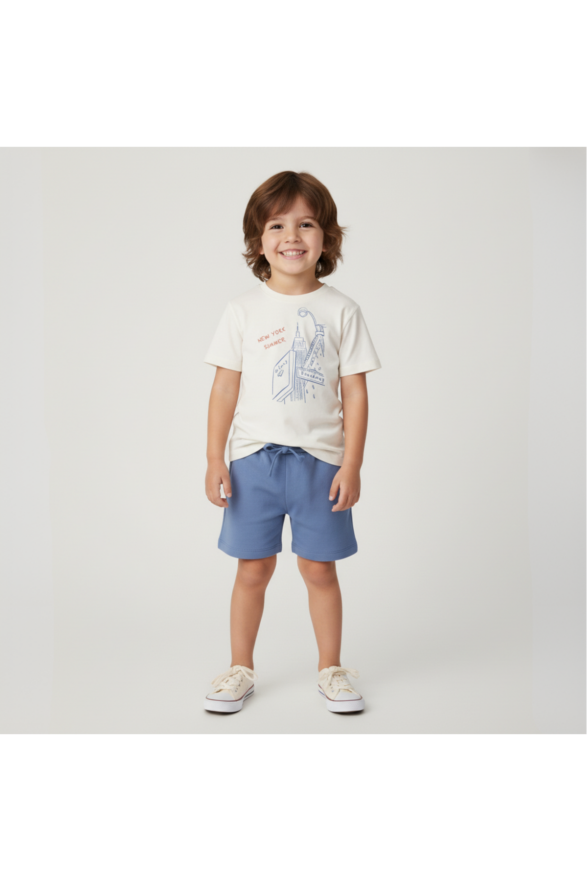 A young child stands smiling, wearing a cream graphic tee featuring a blue New York illustration and light blue shorts.