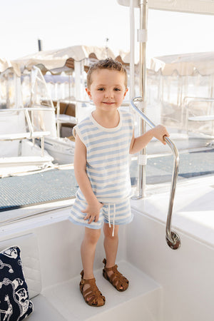 A young child stands on a boat wearing a blue and white striped sleeveless tank and matching shorts, smiling.