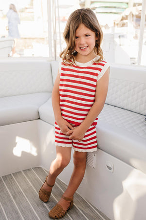 A smiling child stands on a boat, wearing a red and white striped knit tank set. The outfit features a soft, breathable material, perfect for comfortable summer wear.