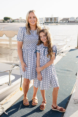 A woman and a girl stand on a boat dock, both wearing matching cotton dresses with a nautical print.