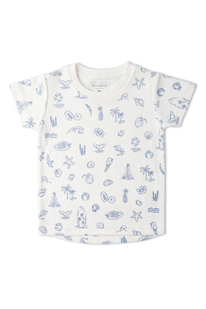 A white short-sleeve tee features a playful coastal print with blue illustrations of seashells, surfboards, and marine life. Made from soft organic cotton, its ideal for summer adventures.