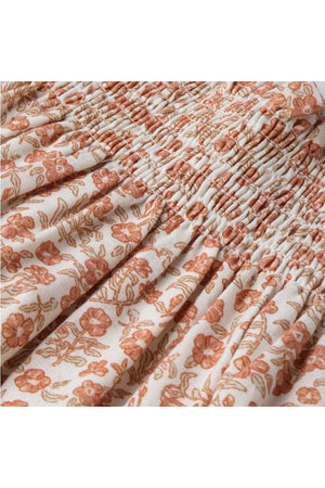 Close-up view of a floral patterned fabric featuring soft orange flowers on a cream background. The material appears lightweight and breathable, ideal for a comfortable summer outfit for children.