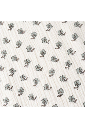 A close-up of a soft, organic cotton muslin fabric featuring a delicate pattern of green and brown cotton plants on a cream background, showcasing its breathable and eco-friendly design.