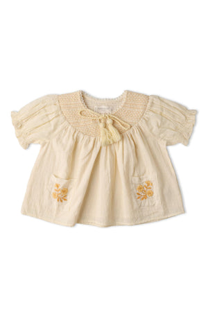 A soft, organic cotton smocked top in butter yellow features short puffed sleeves, a textured weave, and delicate embroidery on the pockets, perfect for sunny day outings.