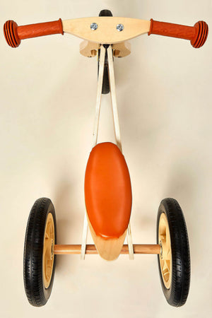 A top view of a 2-in-1 Midi Wooden Balance Bike featuring a natural wood frame, orange seat, and rubber tires.