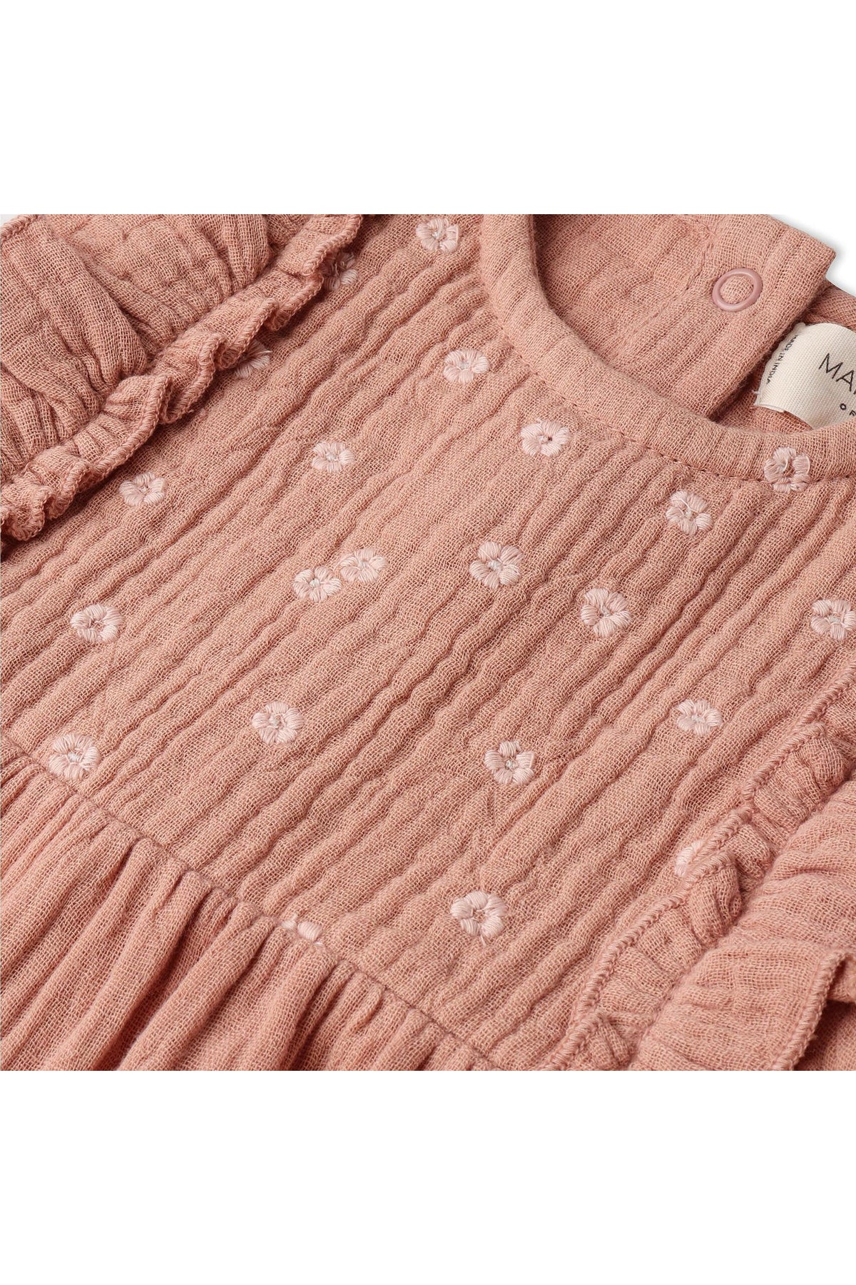 Close-up of a clay-colored organic cotton romper featuring delicate floral embroidery and ruffle accents, designed for comfort and style in warm weather. Ideal for young children.