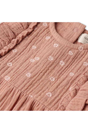 Close-up of a clay-colored organic cotton romper featuring delicate floral embroidery and ruffle accents, designed for comfort and style in warm weather. Ideal for young children.