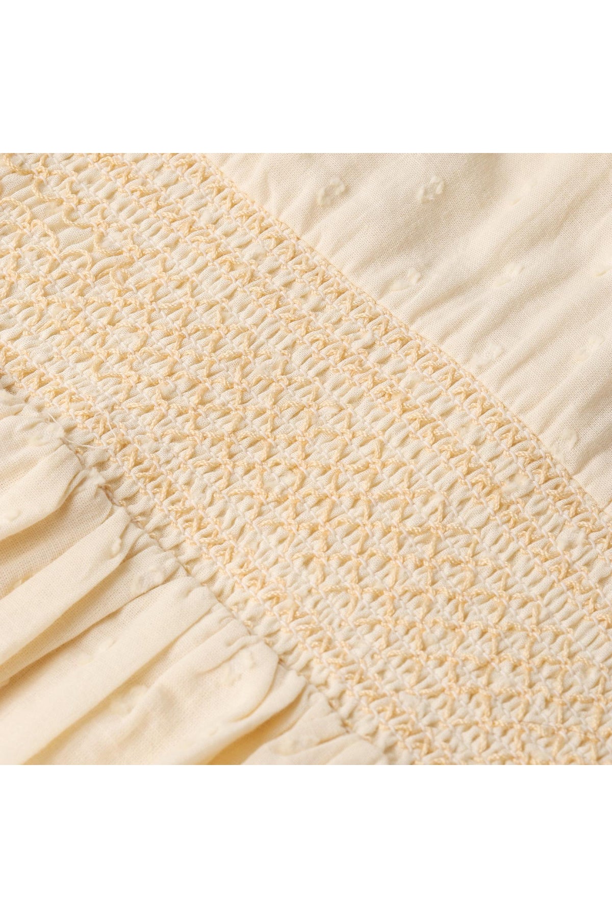 Close-up image of delicate smocking on a butter yellow fabric, showcasing soft organic cotton texture. The intricate stitching adds a vintage-inspired charm to the design, perfect for childrens wear.