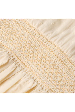 Close-up image of delicate smocking on a butter yellow fabric, showcasing soft organic cotton texture. The intricate stitching adds a vintage-inspired charm to the design, perfect for childrens wear.