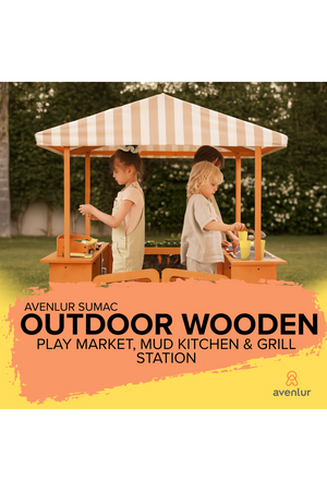 Two children play at the Avenlur Sumac outdoor wooden market and mud kitchen station, featuring a striped canopy and colorful play accessories, set against a lush green garden backdrop.
