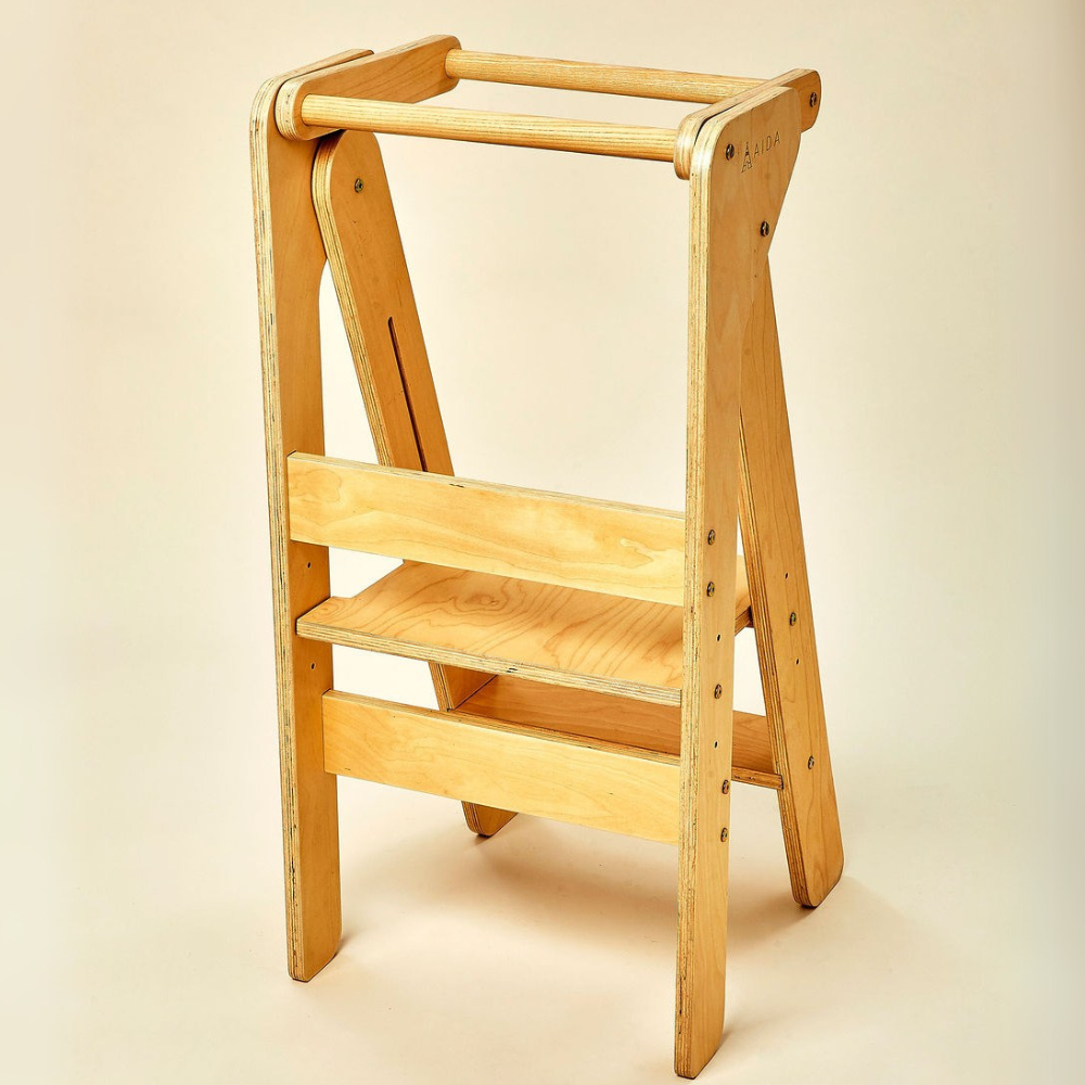 A wooden foldable educational tower with a natural finish features two sturdy shelves and a safety rail. Its designed for children to assist in cooking and daily activities.