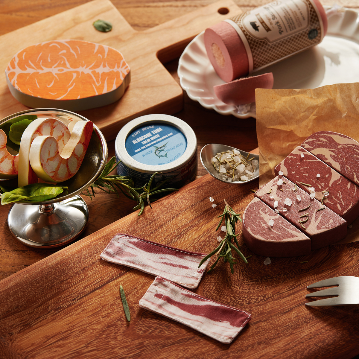 A vibrant wooden play food set features assorted organic meat and seafood items, including salmon, steak, and shrimp, arranged on a rustic wooden surface with fresh herbs and garnishes.