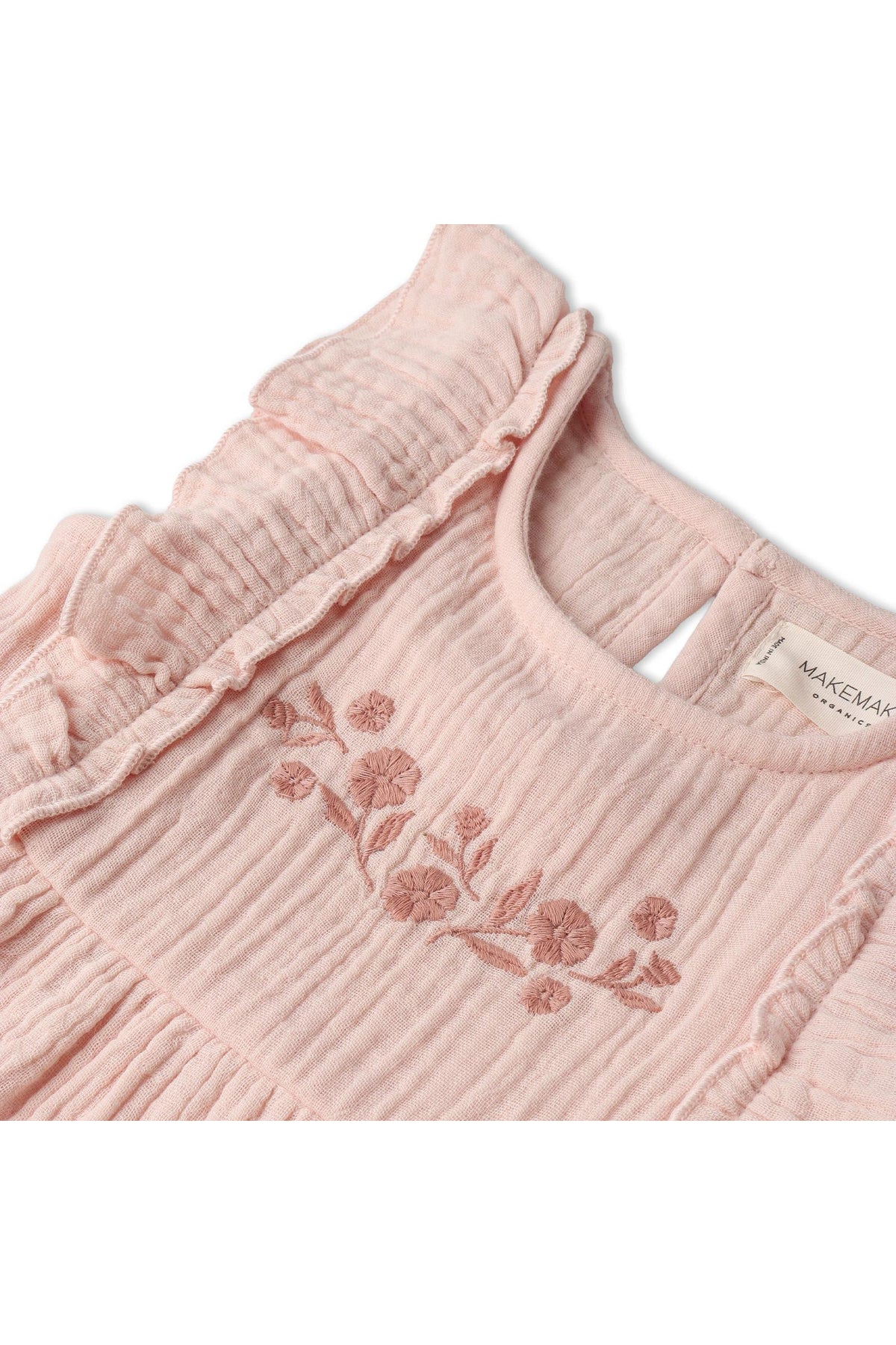 Close-up of a blush-colored organic cotton dress featuring delicate floral embroidery and soft, tiered ruffles. The dress is designed for children, emphasizing a sustainable and charming aesthetic.