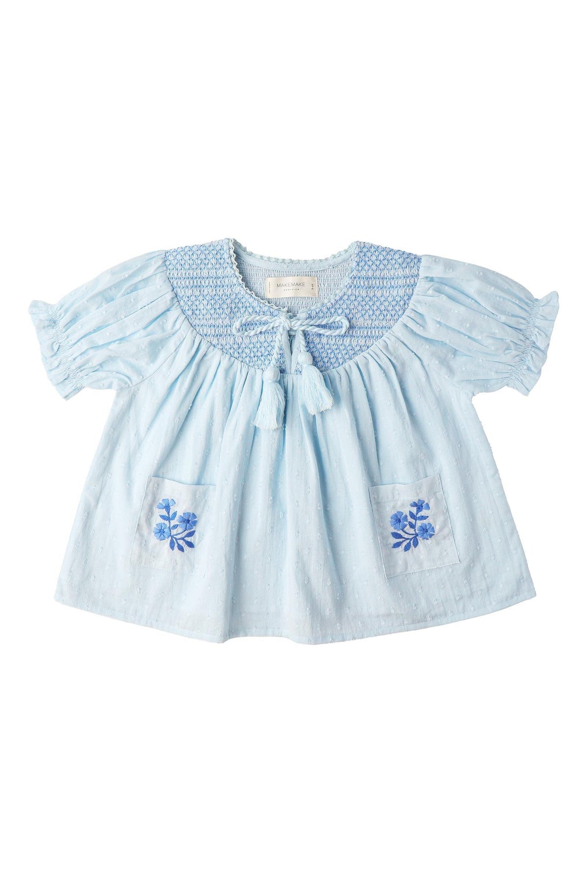 Light blue organic cotton smocked top featuring delicate embroidery on the pockets and a textured dobby weave. Designed for comfort, it is perfect for sunny day outings.