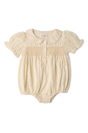 A butter yellow organic cotton romper features a smocked bodice, puff sleeves, and classic wooden buttons. This airy, soft piece is perfect for warm days and playful adventures.