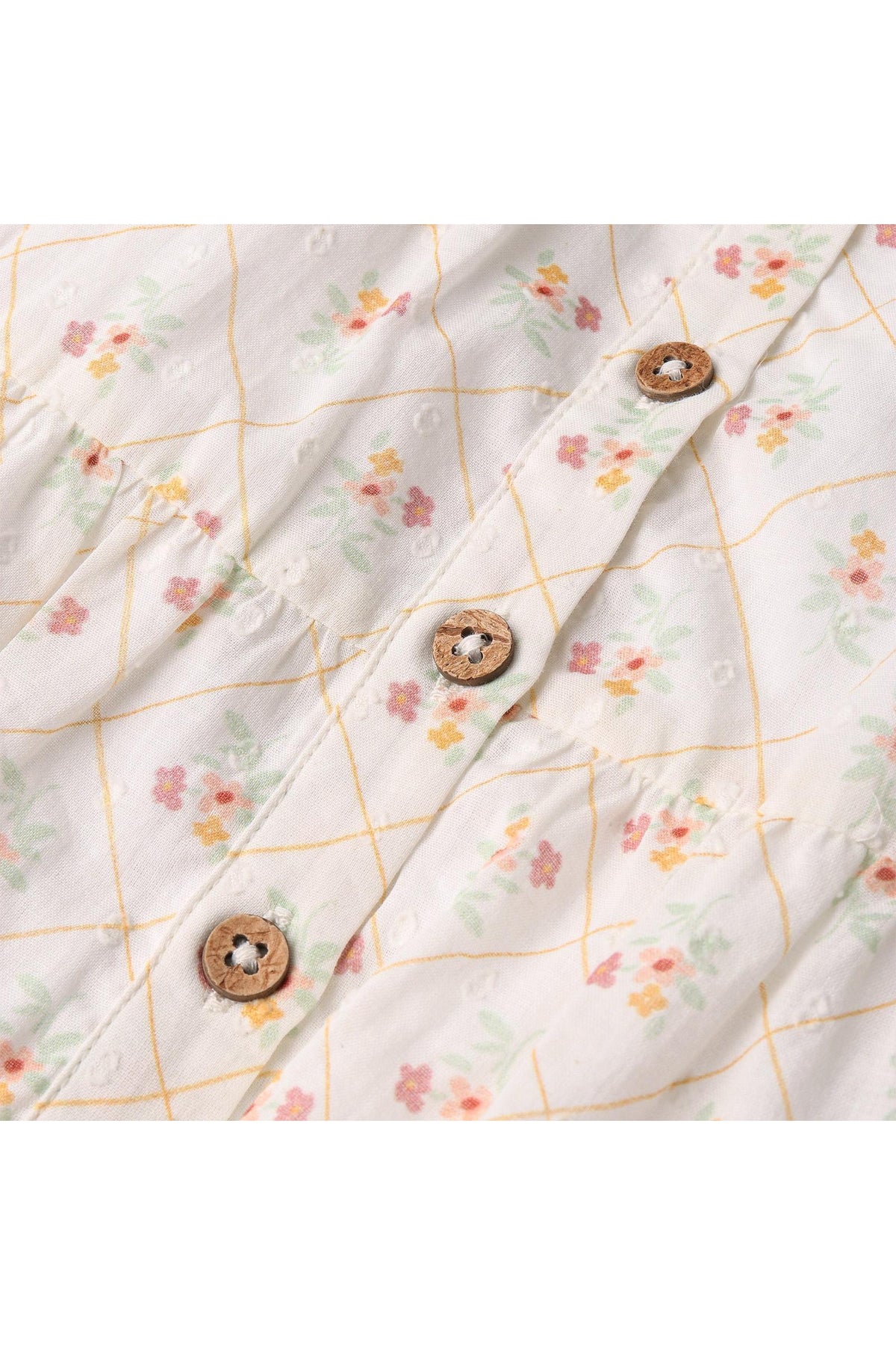 Close-up of a lightweight, floral-patterned fabric showcasing soft pastel flowers and a grid design, featuring wooden buttons that enhance the organic aesthetic of the dress. Ideal for spring wear.