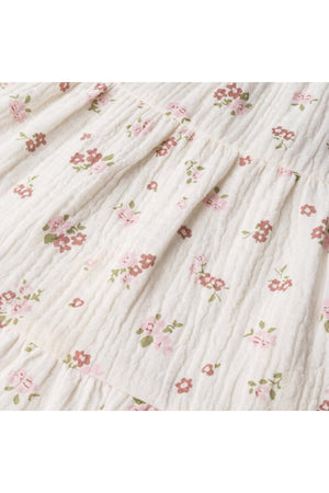 Close-up view of a soft, organic cotton fabric featuring a blush floral pattern with pink and green flowers on a white background, showcasing the gentle smocking detail of the jumpsuit.