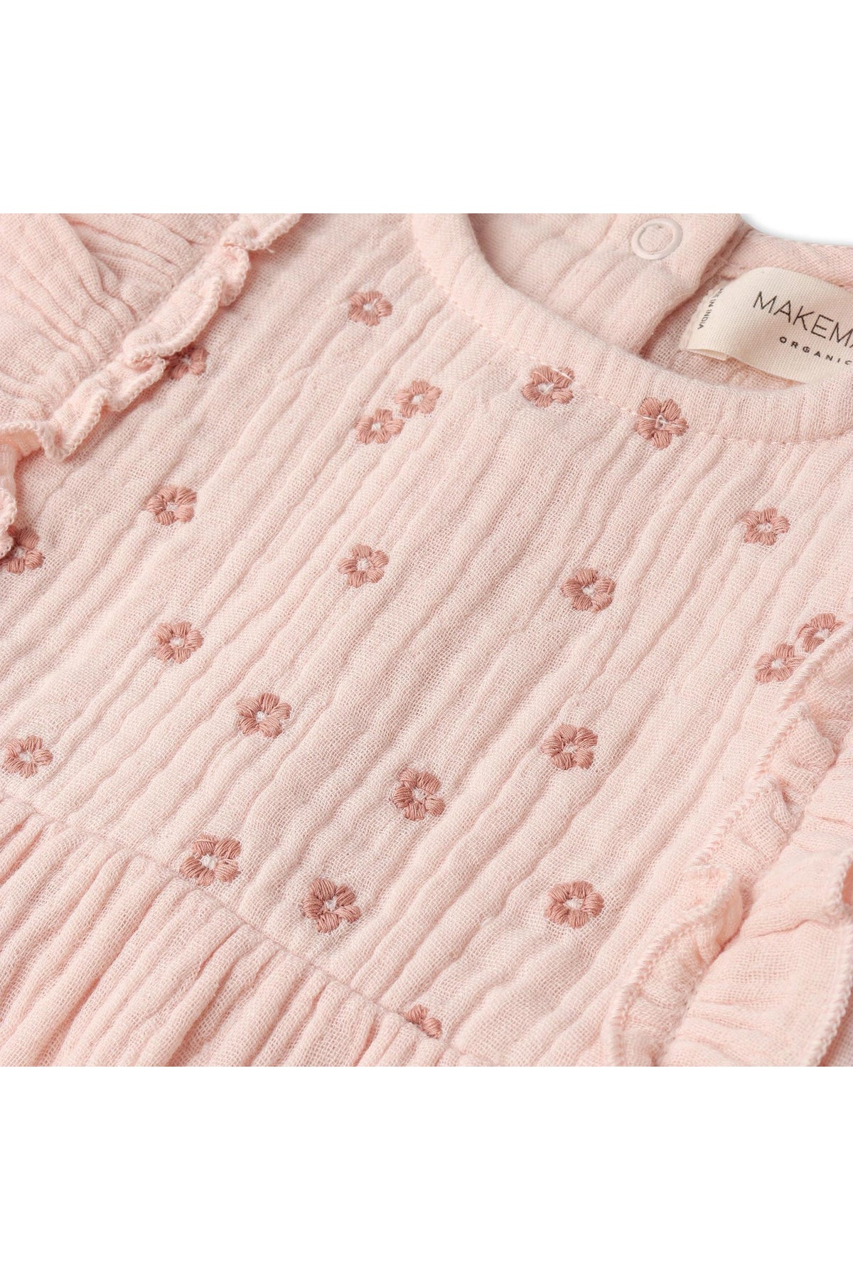 Close-up of a soft blush romper made from organic muslin cotton, featuring delicate ruffle accents and intricate floral embroidery, ideal for warm-weather days and gentle on the skin.
