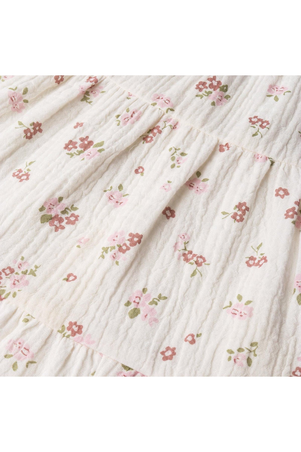 Close-up view of a light cream fabric featuring delicate pink and green floral embroidery. The textured material gives a soft, organic feel, suitable for children’s clothing.