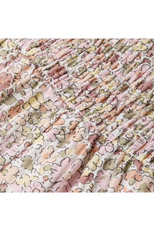 Close-up view of soft, organic cotton fabric featuring a pastel floral print with gentle smocking details. The delicate design is perfect for lightweight, breathable clothing for children.
