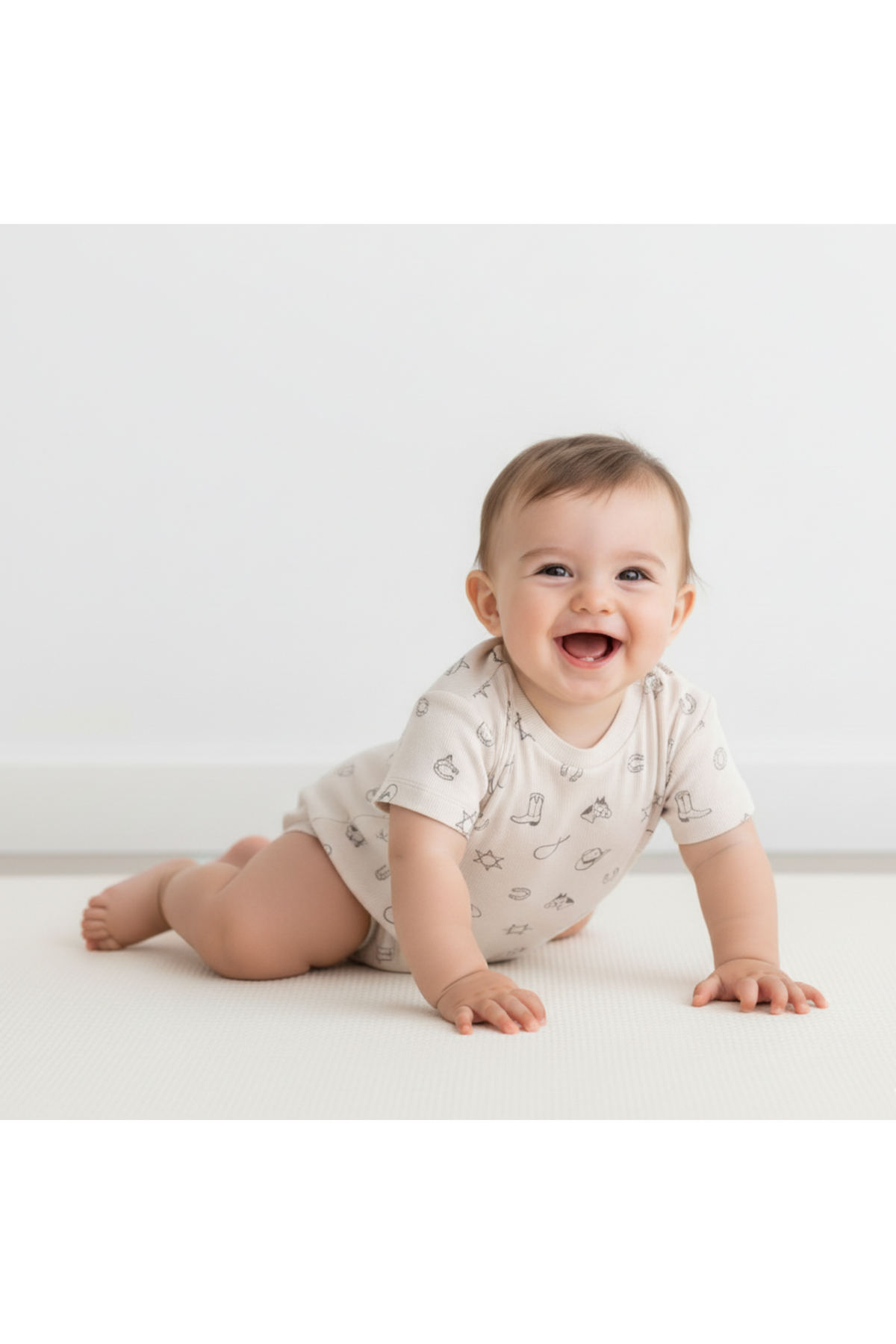 A smiling baby crawls on a light-colored mat, wearing a cream organic cotton romper adorned with playful, simple patterns. The romper offers comfort and style for little explorers.
