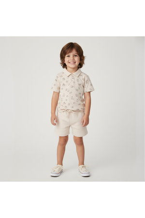 A smiling child wears a beige organic cotton Collar Tee and matching shorts, featuring playful rodeo prints. The outfit is perfect for sunny day adventures and promotes sustainable fashion.