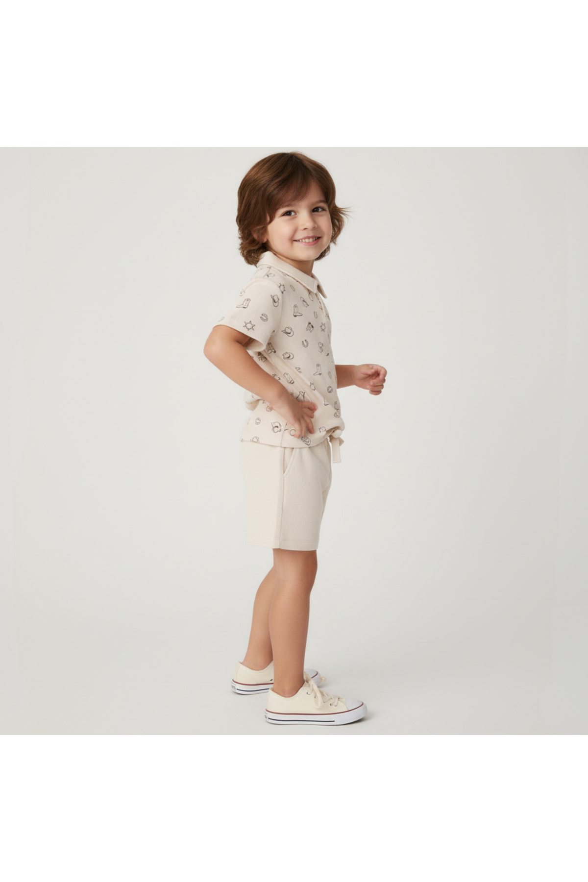 A child stands sideways, wearing a beige organic cotton collar tee with a playful print and matching shorts. The outfit is stylish and perfect for sunny day adventures.