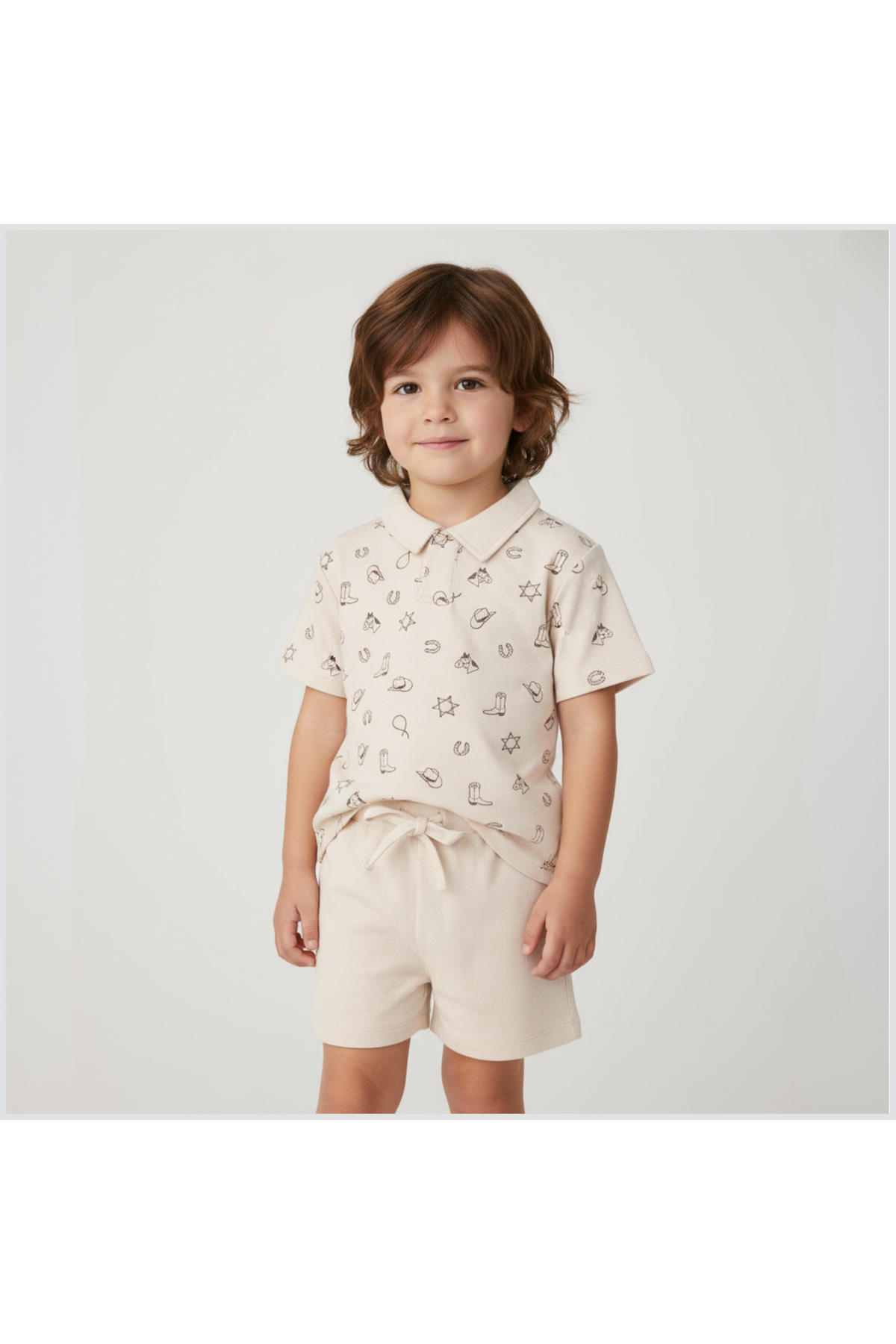 A young child stands smiling, wearing a beige organic cotton collar tee with playful patterns and matching shorts.