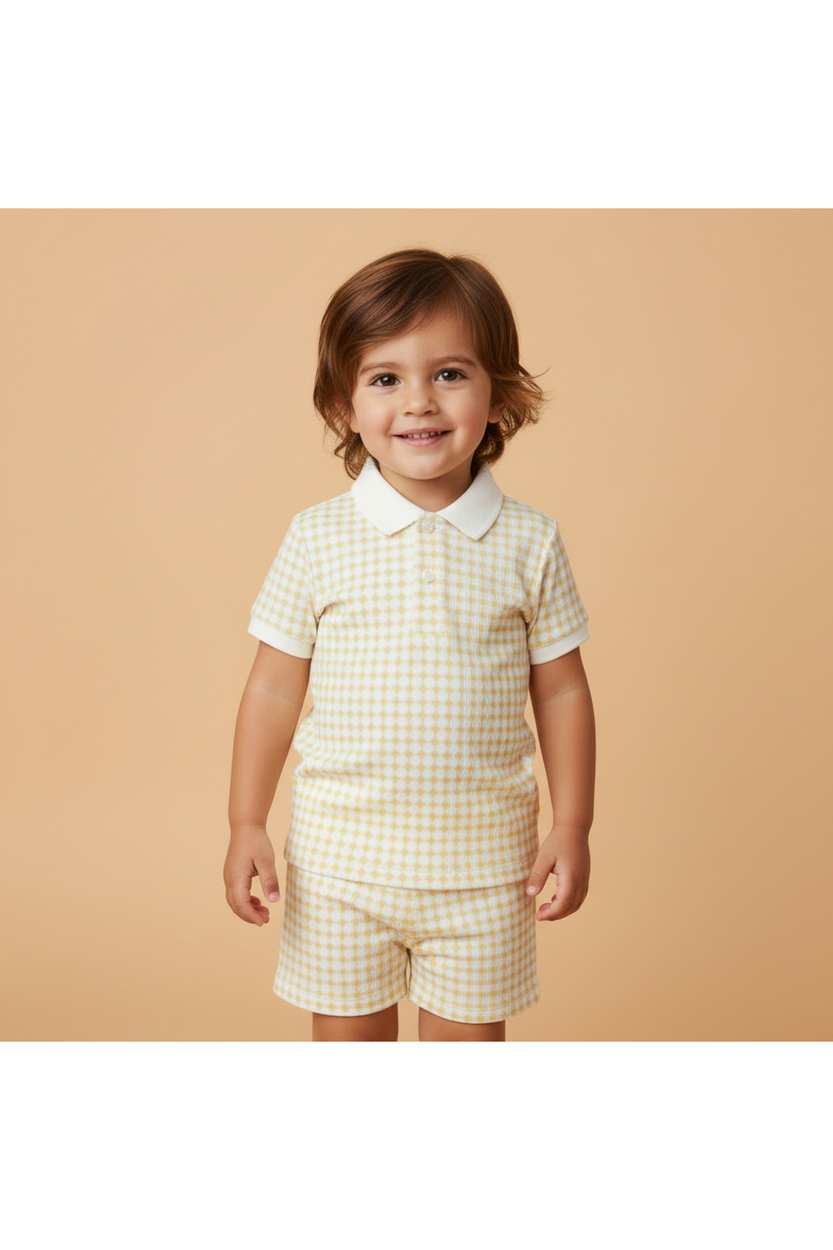 A smiling child wears a light yellow gingham collar tee and matching shorts, made from soft organic cotton. The background is a warm beige, enhancing the cheerful, playful vibe.
