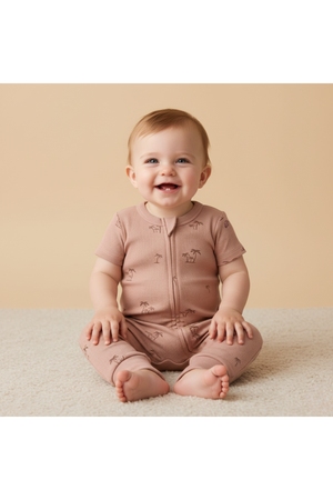 A smiling baby sits on a soft beige surface, wearing a light pink organic cotton romper featuring subtle animal patterns and a two-way zip closure, highlighting comfort and style.