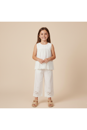 A young girl smiles while wearing an ivory organic cotton eyelet top with a flowy silhouette and matching pants featuring intricate cutwork.