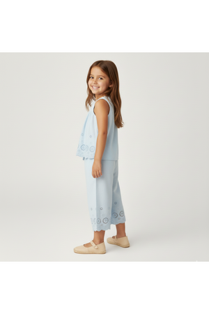 A young girl is smiling while wearing a light blue organic cotton eyelet top and matching pants set.