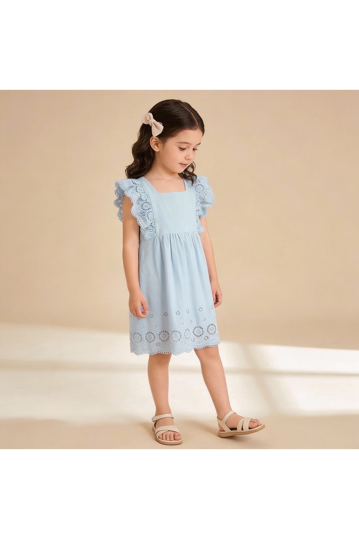 A young girl stands in a light blue organic cotton dress with delicate flutter sleeves and embroidered eyelet details. The soft fabric is perfect for comfortable, stylish playdates.